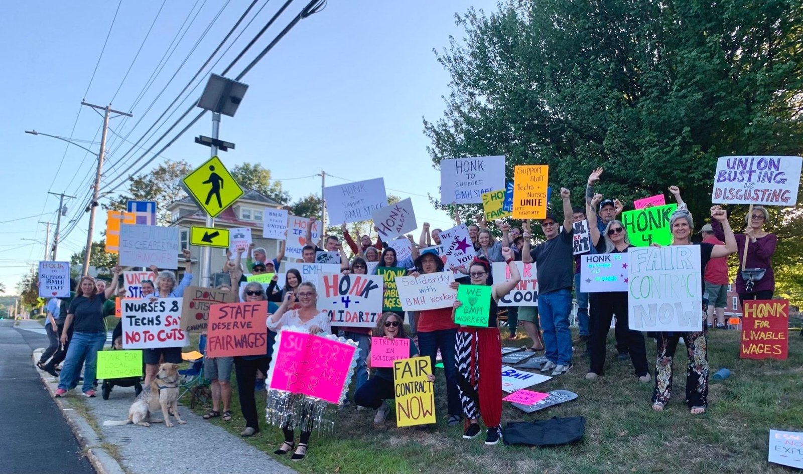 A group of people outdoors with signs reading “Fair contract now,” “Staff deserve fair wages,” and “Union busting is disgusting.”
